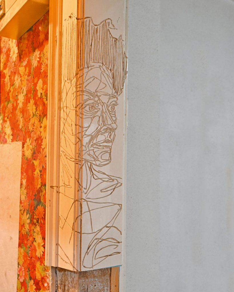 Geritztes Graffiti von Michael Genter, darunter hat Udo W. Hoffmann ein Stück der Türrahmenfassung weg gesägt.